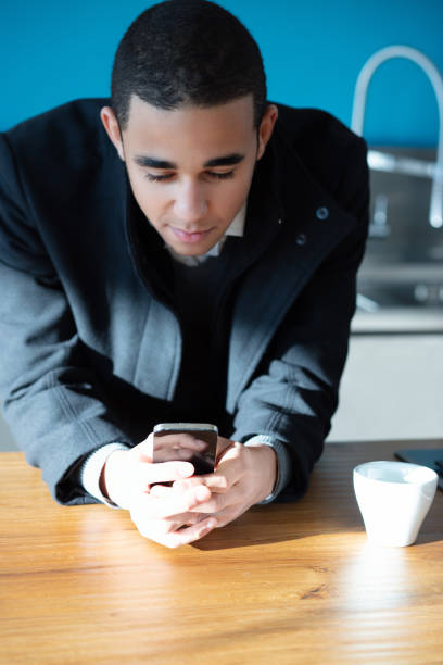 Serious young businessman using smartphone indoors, browsing internet and checking messages in natural light