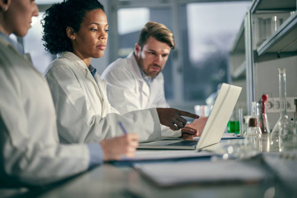 Team of young scientists working on a computer in laboratory. African American female chemist and her colleagues cooperating while working on laptop in laboratory. Copy space. biochemist stock pictures, royalty-free photos & images