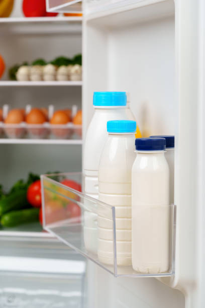 A white refrigerator is open, revealing a well-stocked interior with fresh fruits, vegetables, eggs, and other groceries.