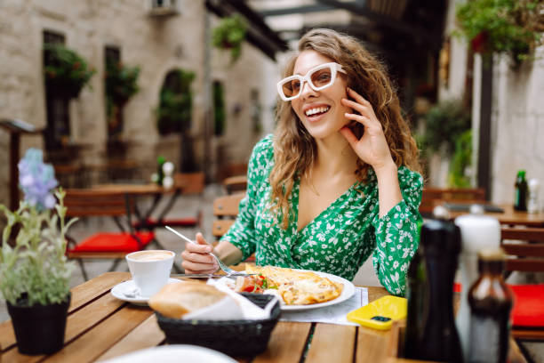 Young woman using mobile phone while walks with a bicycle and looks around at beautiful architecture. Young woman sitting in a street cafe eating italian pasta and drinking coffee and watching the city life, Europe lifestyle. Tourism, food and drink. mediterranean woman portrait stock pictures, royalty-free photos & images
