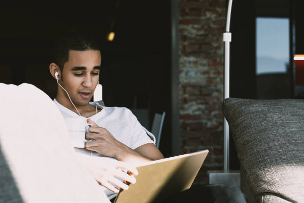 istock Young man relaxing on sofa listening to music and reading on tab 2161574431