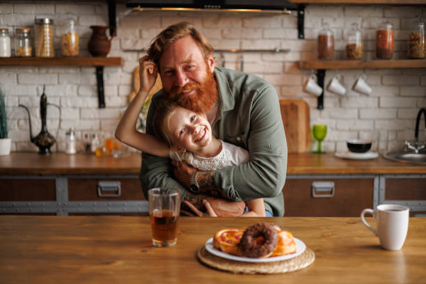 istock Smiling father hugging daughter and looking at camera near breakfast in kitchen 2161580811