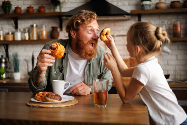 Tattooed father having fun with daughter and pastry during breakfast in kitchen