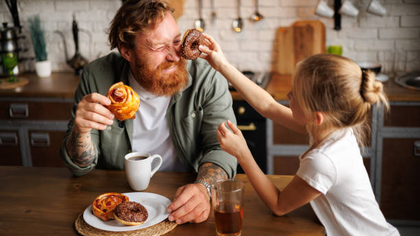 istock Daughter holding donut near tattooed father while having fun in kitchen 2161580887