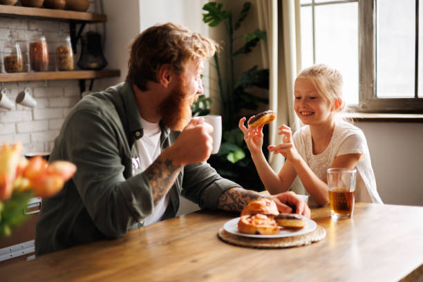 istock Smiling child holding donut while talking to father with coffee during breakfast in kitchen 2161580895