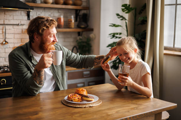 istock Smiling father looking at daughter with donut during breakfast in kitchen in morning 2161580920