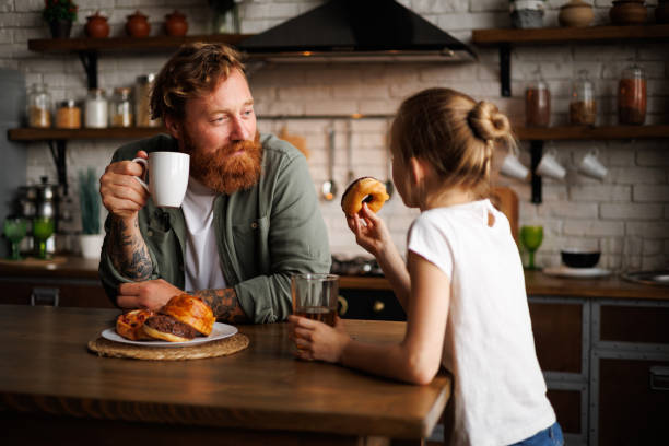istock Smiling father holding coffee while daughter eating donut in morning in kitchen 2161580925