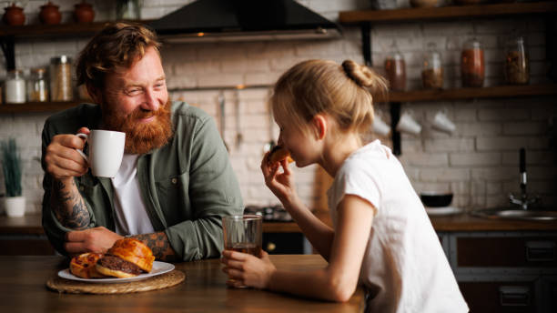 istock Tattooed father holding coffee while daughter holding donut during breakfast in kitchen 2161580945