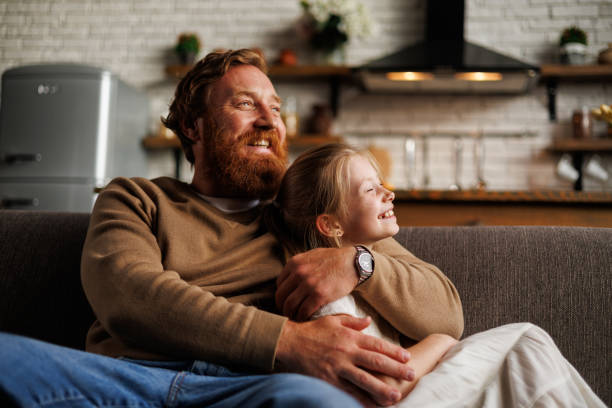 istock Cheerful bearded father hugging preadolescent daughter while relaxing on couch together at home 2161582157