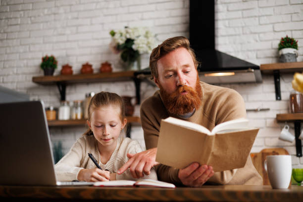 istock Father reading book while supporting daughter with online education in kitchen at home 2161582598