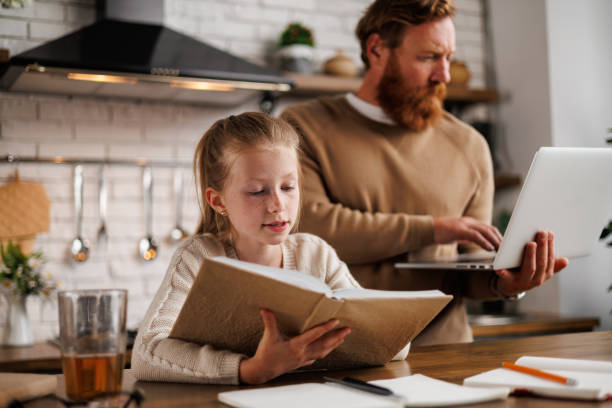 istock Kid reading book near father with laptop and notebooks during home-based learning in kitchen 2161582654