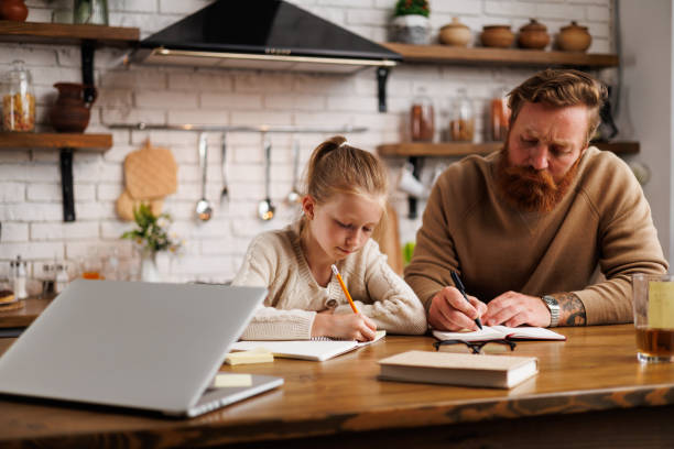 istock Kid writing on notebook near father and laptop in kitchen during online education 2161582847