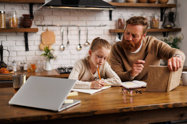 istock Father holding book while daughter doing homework near laptop in kitchen at home 2161582876