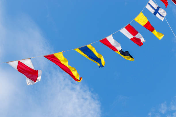 A vibrant Catalan flag flutters in the wind against a backdrop of a clear blue sky. The flag's distinctive red and yellow stripes stand out against the natural elements. The image captures the maritime heritage of Catalonia.