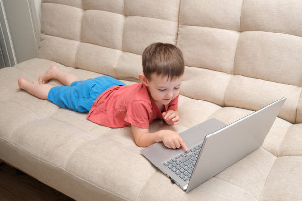 istock A young boy is laying on a couch and using a laptop. Kid aged 3 years (three year old child) 2161599828