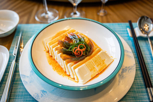 This image showcases a meticulously prepared homestyle braised tofu dish. The thick slabs of tofu are carefully arranged on the plate, topped with slivers of chili peppers and sprigs of cilantro, creating a visually striking and appealing presentation.
