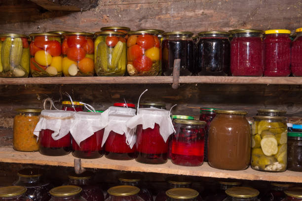 Glass jars of canned vegetables and jam sit on shelves in the basement of a village house.