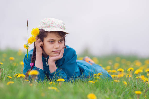 The girl lies on the green grass with yellow flowers.