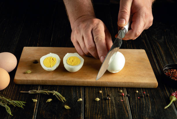 istock A man hands cutting a hard-boiled egg in half on a wooden surface next to another hard-boiled egg, already cut, with a yellow yolk in view 2161608245
