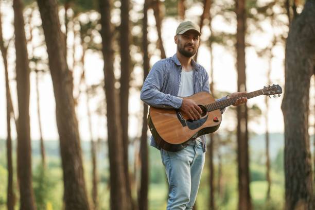 Handsome man is in the forest with acoustic guitar.