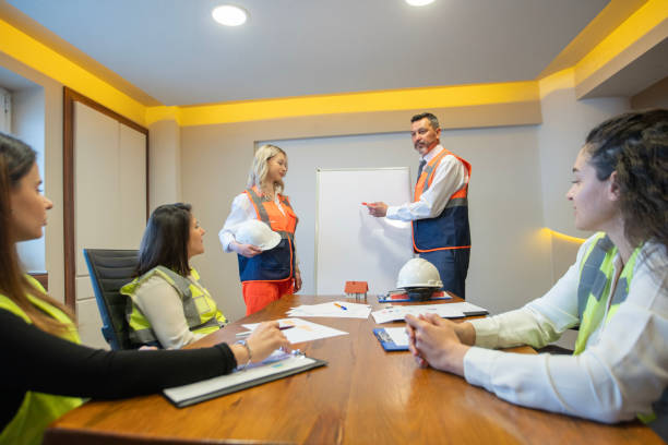 istock Male Engineer Presenting at Whiteboard and Female Engineer Holding Hard Hat 2161617041