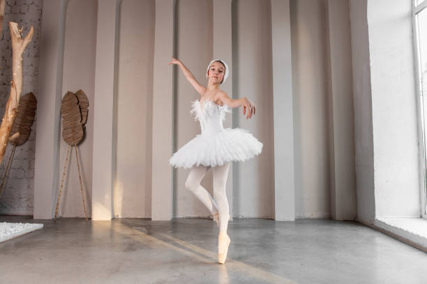istock Elegant young ballerina performs beside large windows, poised stance, delicate white tutu 2161617764