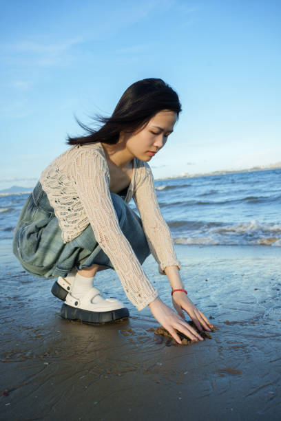 istock Asian girl squatting on the beach 2161617913