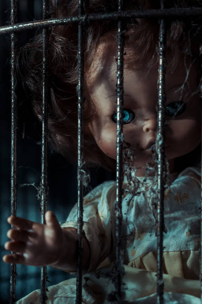 Creepy doll with blue eyes trapped behind rusty bars. Halloween theme.