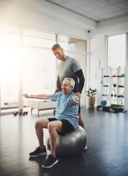 istock Stretching, senior man and physiotherapist with band for resistance training, support or muscle workout. Fitness, physiotherapy and happy elderly person with ball for mobility exercise in retirement 2161632241