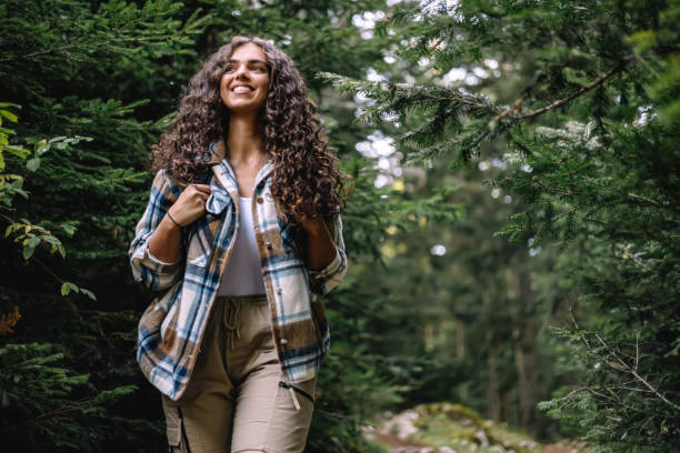 istock Curly-haired woman smiling while hiking through forest 2161634380