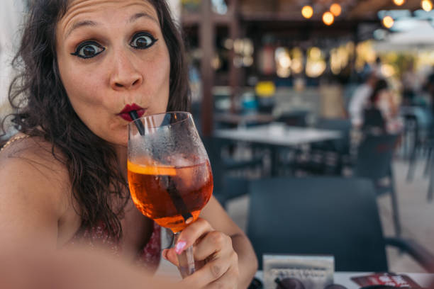 istock Gesturing woman taking selfie while drinking spritz cocktail. Woman enjoying a refreshing spritz cocktail while taking a selfie on a beach bar 2161638371