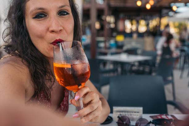 istock Smiling woman taking selfie while drinking spritz cocktail. Woman enjoying a refreshing spritz cocktail while taking a selfie on a beach bar 2161639078