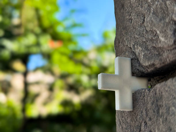A beautifully captured image showcasing a white cross embedded in a stone wall, with a lush, green blurred background.