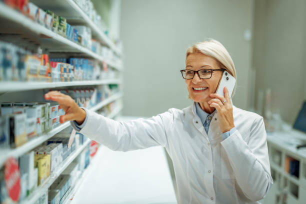 istock Mature female pharmacist talking on smart phone while working at pharmacy store 2161650837