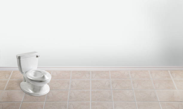 A roll of white toilet paper sits on the edge of a modern toilet in a well-lit bathroom. The tiles have a subtle texture, and droplets of water are visible on the wall.
