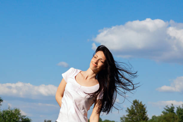 beautiful brunette stands in the wind on a summer day against a clear blue sky