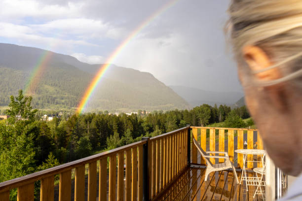 Young woman looks at double rainbow over forest from deck
