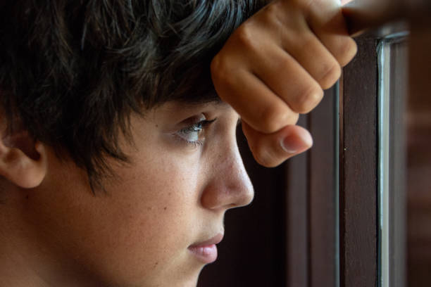 Pensive Caucasian teenage boy looking through a window