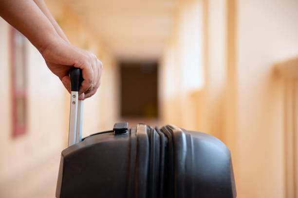 istock Close-up of hand pulling black suitcase with retractable handle down hallway, evoking sense of travel and departure 2161684719