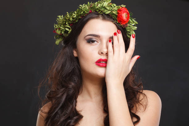 Nice young woman with floral head wreath looking at camera while standing against black background