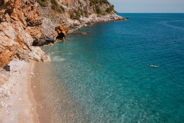 A teenage girl is having fun on the paddleboard surrounded with rocky coast.