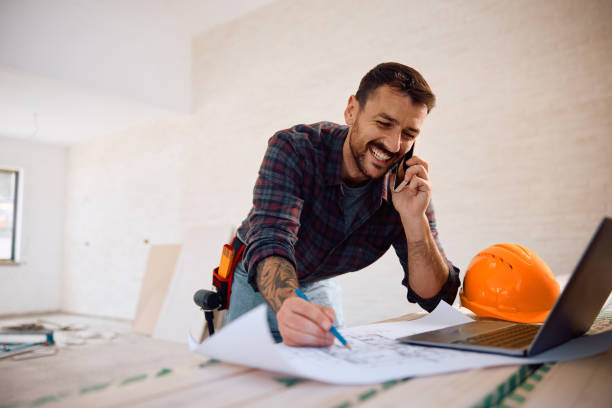 istock Happy worker talking on the phone while examining housing plans at construction site. 2161686861