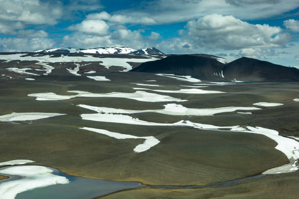 Aerial shot of the dramatic volcanic landscape of the central Highlands of Iceland on a sunny day in summer, where patches of snow are still clinging to the barren ground.
