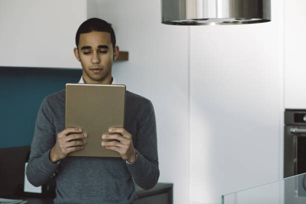 istock Focused young man reading news on a tablet in a kitchen 2161697815