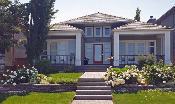 Calgary, Alberta, Canada- July 11,2024: Front view of new modern home. Peonies in front garden. July. Different design. Red glass Door. Large entrance. Aggregate Sidewalk up to entrance.