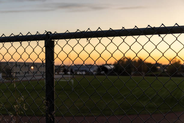 Sunset hues backlighting a chain-link fence - golden hour sky gradient transitioning from warm orange to cool blue - silhouette of urban skyline in the distance. Taken in Toronto, Canada.
