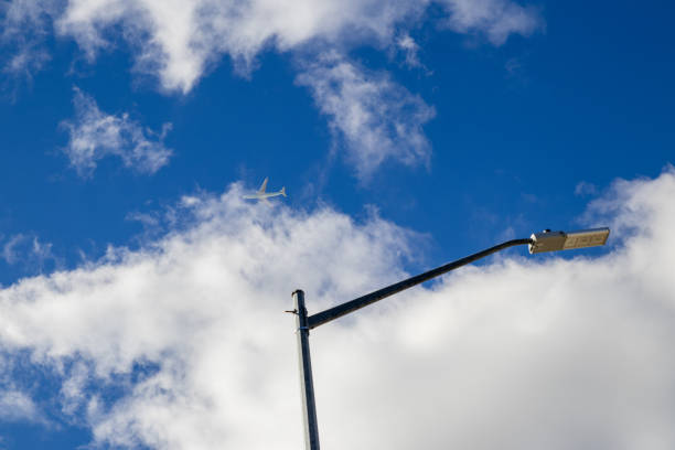 Clear sky backdrop - fluffy white clouds - commercial airplane mid-flight - street lamp foreground. Taken in Toronto, Canada.