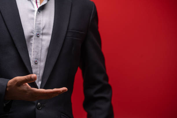 Male hand in a suit shows a palm up gesture on a red background.