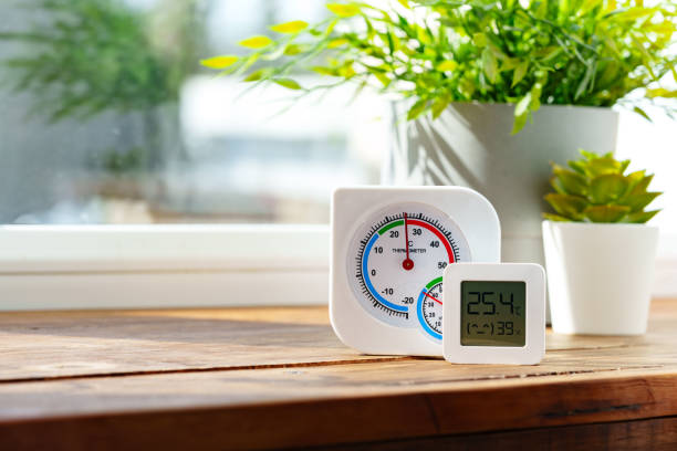 This image shows a digital thermometer sitting on a wooden table in front of a window.