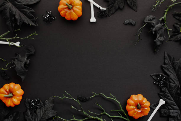 istock Halloween flat lay composition with orange pumpkins, spooky white bones, spiders, branches with bats, and dark foliage on a black backdrop 2161719706